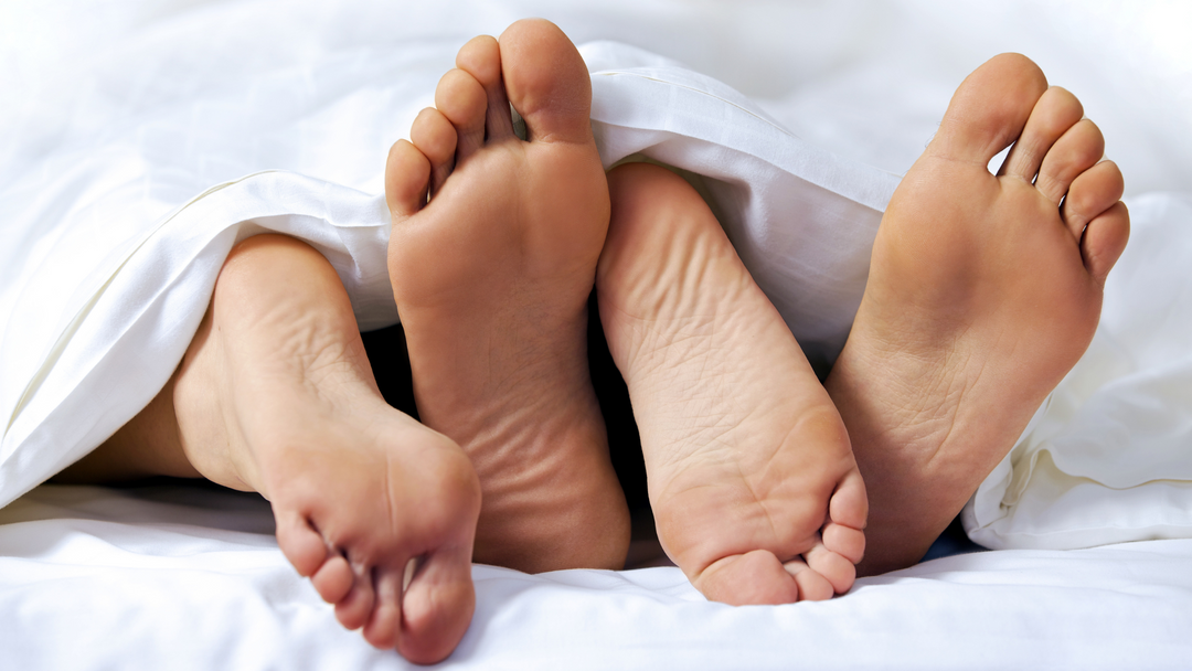 Piedi di una coppia che escono dalle coperte di un letto